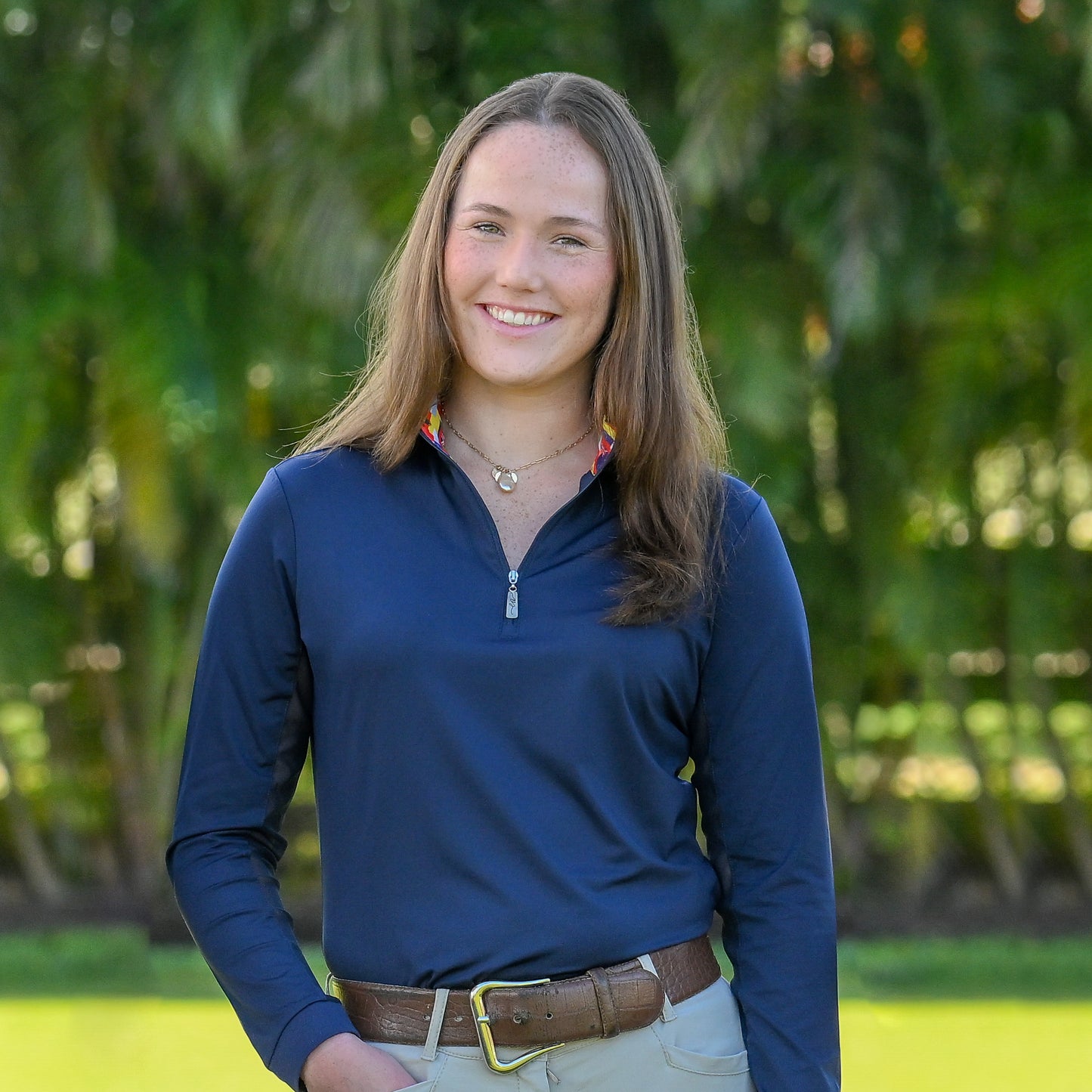 Smiling young woman showcasing the navy International Sun Shirt by EA Limited Inc., with a quarter zip design, UPF 50+ sun protection, and a collar lined with international flags print.