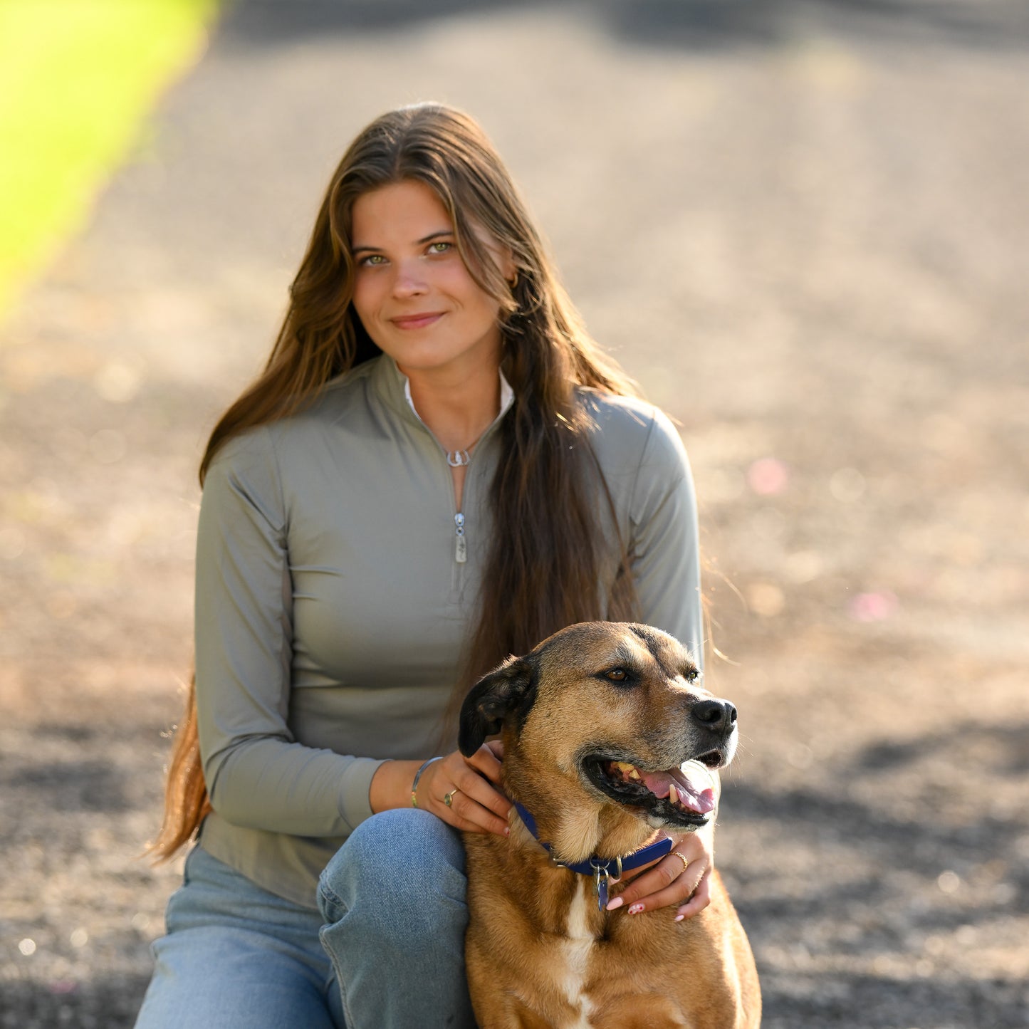 A young woman wearing EA Limited Inc.'s Gray/White Contrast Collar Sun Shirt with a quarter zip, rated UPF 50+, happily posing with her dog.