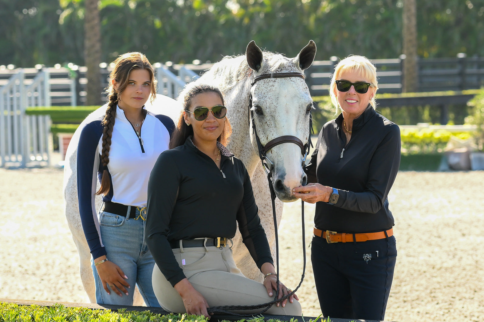 Three female equestrians wearing EA Limited Inc. UPF 50+ sun shirts, confidently posing with a beautiful horse, showcasing their stylish sun protection.