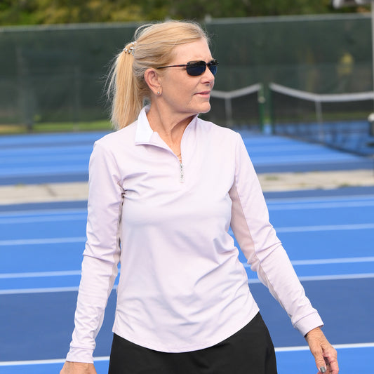 Female tennis player striking a pose in her Lilac/White Contrast Collar Sun Shirt by EA Limited Inc., featuring a quarter zip and a UPF 50+ rating for sun protection.